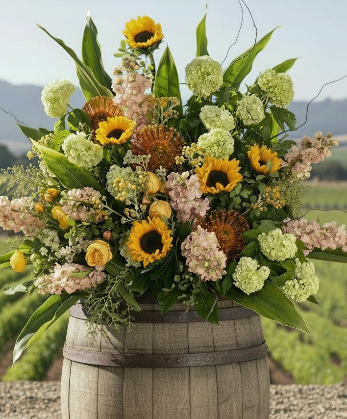 sunflowers, stock, protea, roses arrangement on a wine barrel